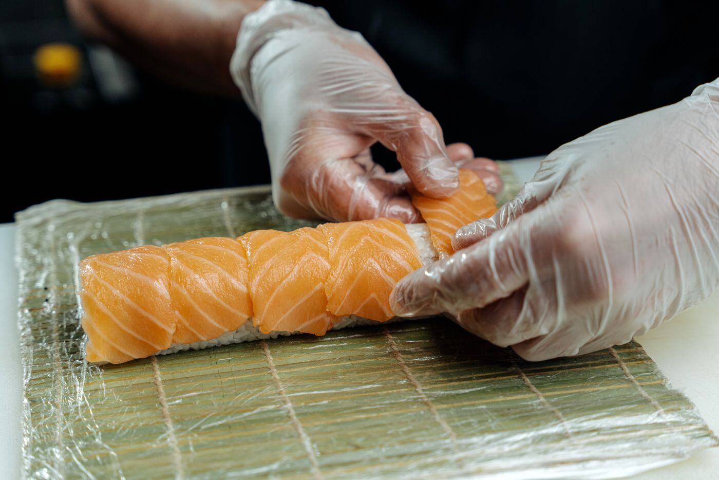 Sushi chef hand-rolling salmon maki at a live catering station