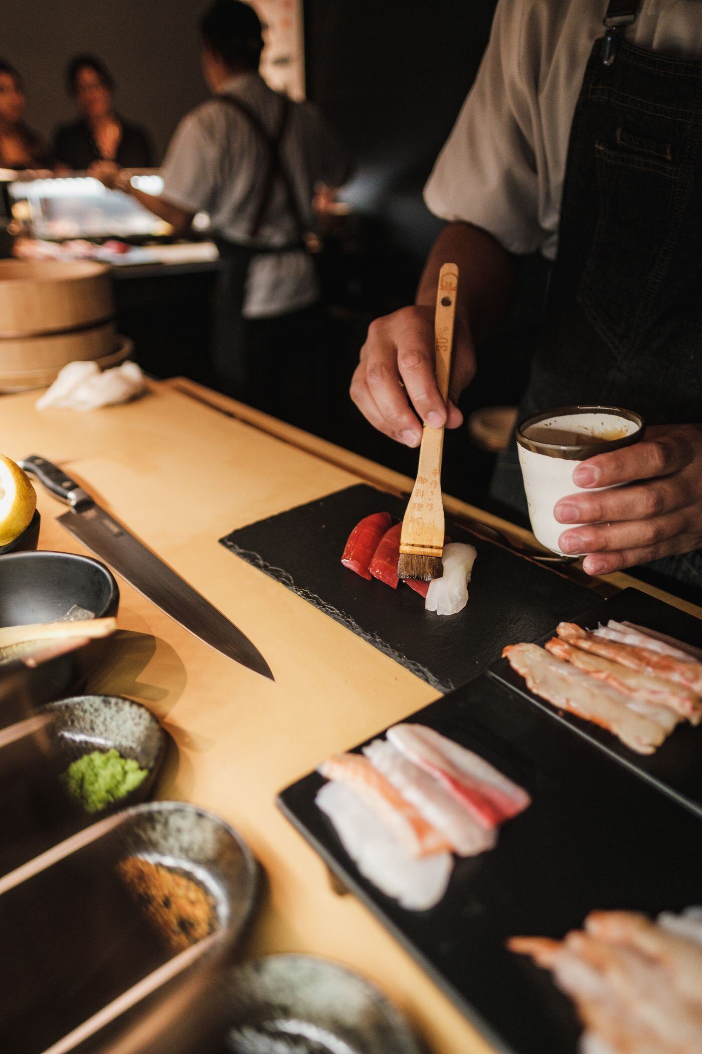 Chef brushing nikiri glaze onto nigiri at a live omakase station