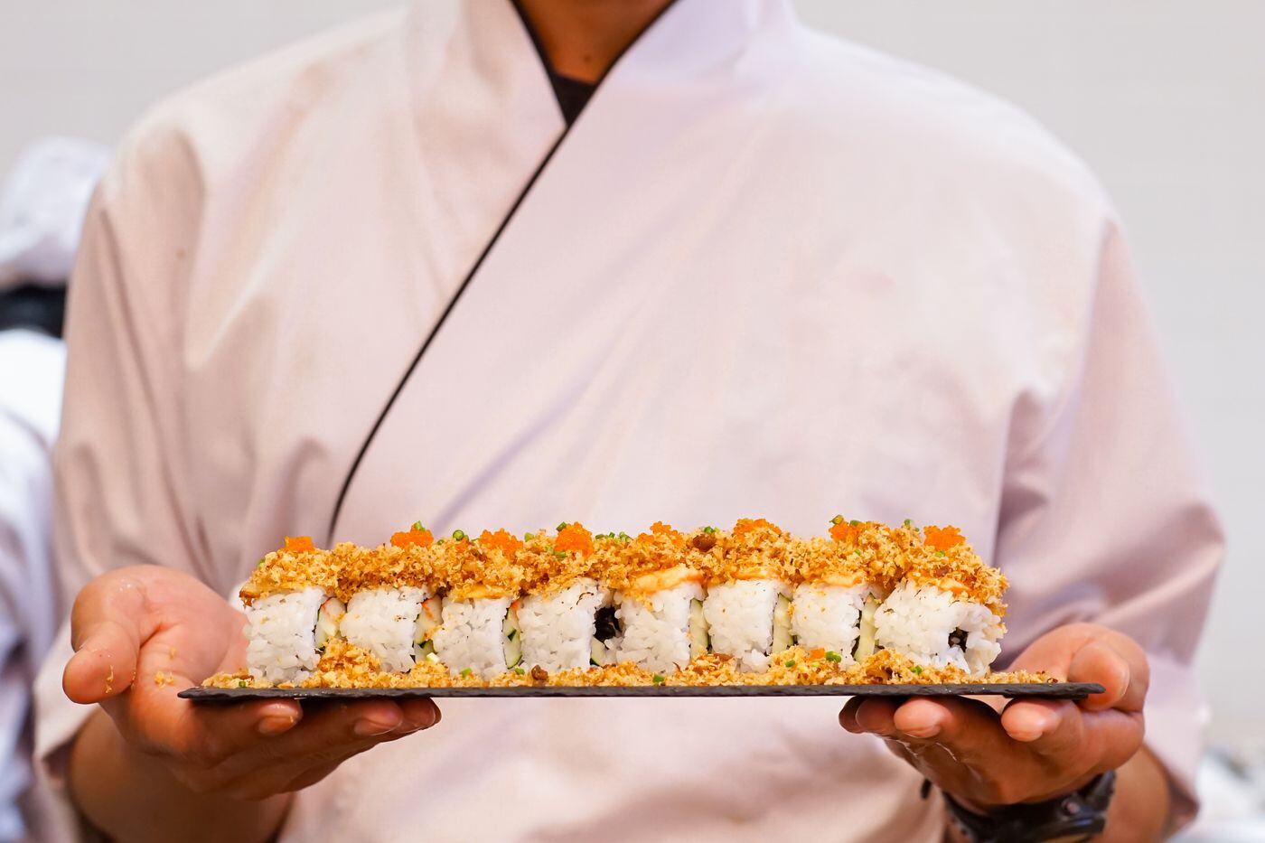 Sushi chef presenting a freshly made signature roll to guests at a NYC event