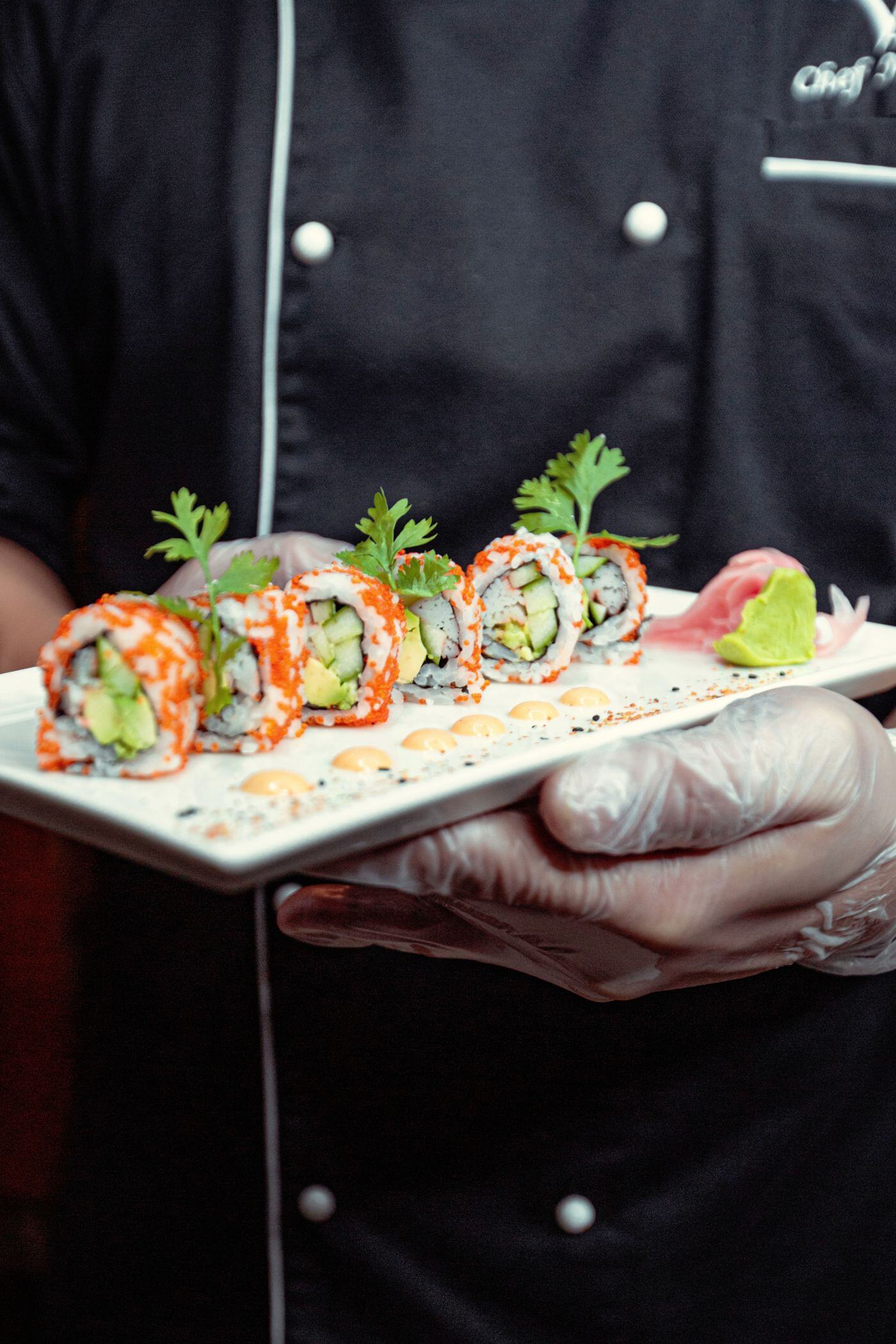 Sushi chef in black uniform serving a plate of signature rolls at a private party