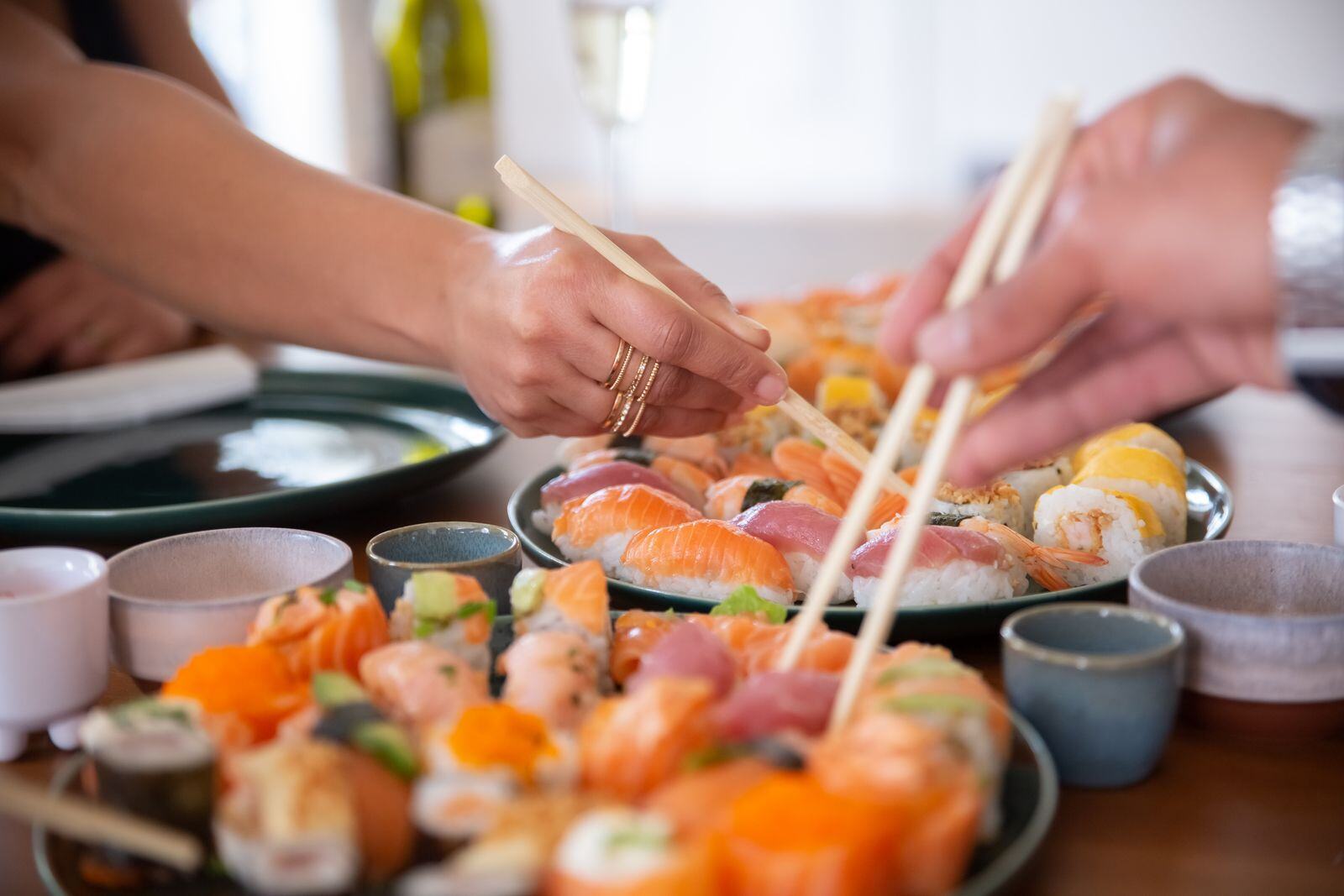 Party guests reaching for sushi from a platter with chopsticks